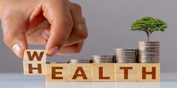 Hand flips the wooden cube with the word wealth for health with a growing pile of coins