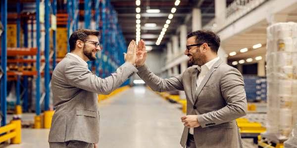 Two businessmen giving high five for successful business while standing in storage