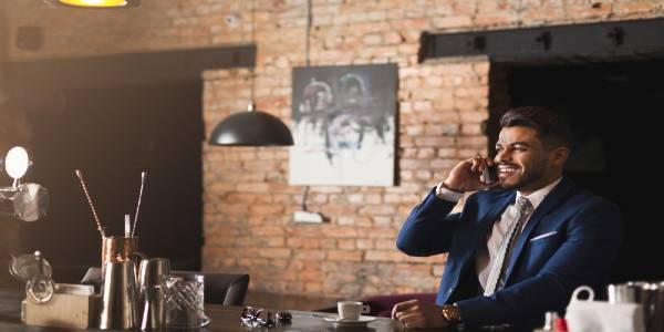 Cheerful business talking on phone, sitting at bar counter in restaurant, drinking espresso and having pleasant conversation, copy space