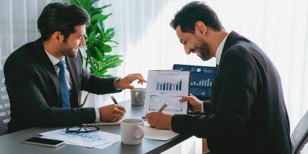 Two men sitting at a table, one of them is looking at a chart of the company's financial data