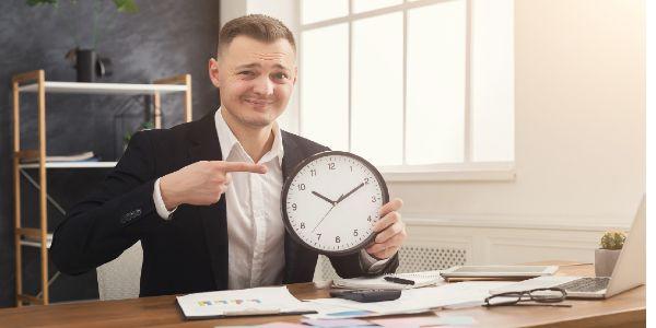 Businessman in suit holding clock and pointing on it. Time management and lack of time concept