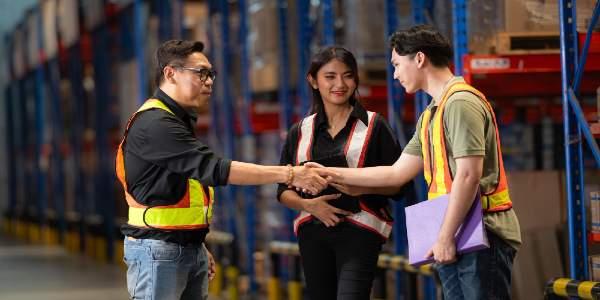 A group of people in warehouse and two men shaking hands and inspecting products on warehouse shelvesare sent to retailer