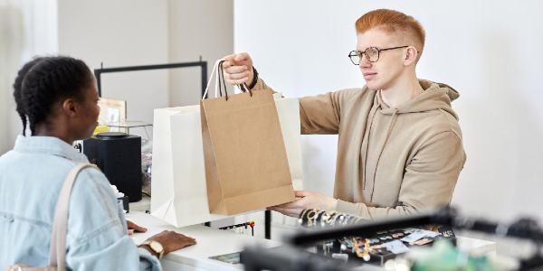 Portrait of male store manager handing paper bags with purchases to customer over counter