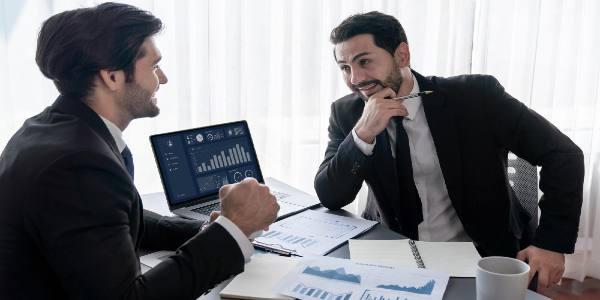 Two men in suits are having a meeting in front of a laptop