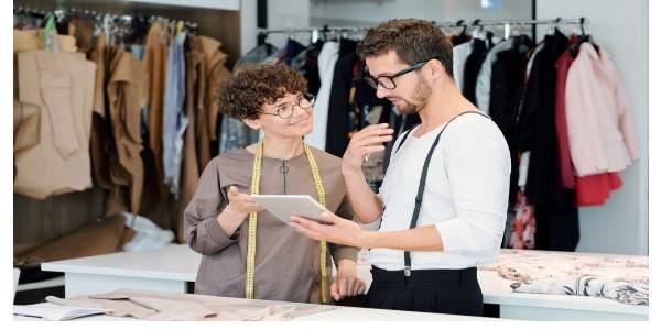 Young clothing designers discussing details of new digital sketches for their fashion collection in touchpad