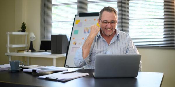 Happy mature man raising his fist in victory and looking at a laptop screen