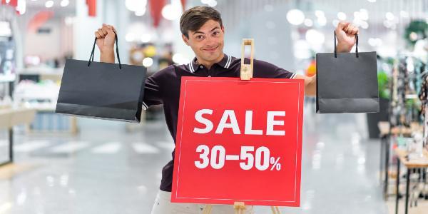 Young smiling guy posing and holding colored bags. Sale and discounts up to 30-50 percent
