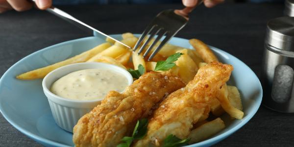 Woman eating fried fish and chips on dark table
