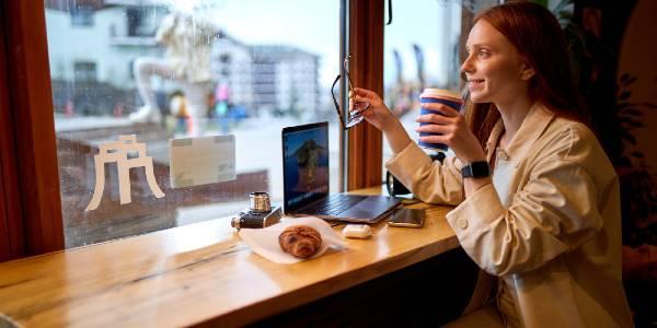 Smiling pretty hipster woman using modern laptop in cafeteria